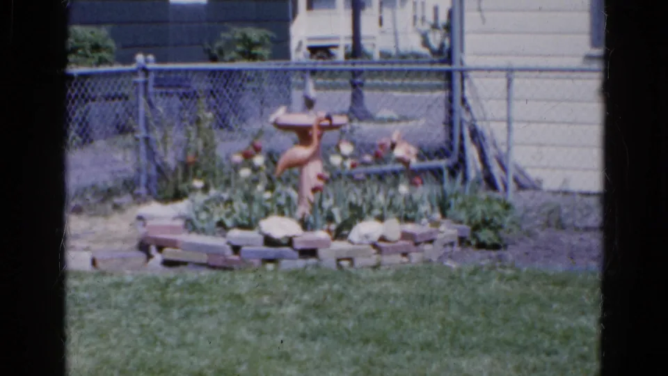Wauconda, Illinois home-movie frame with a maintained backyard garden, lawn, bird bath, and chain-link fence.