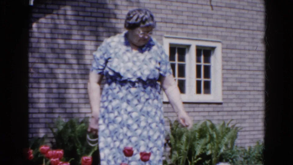 The woman looks down toward the garden while holding a leash outside a brick house in Wauconda, Illinois, 1961.