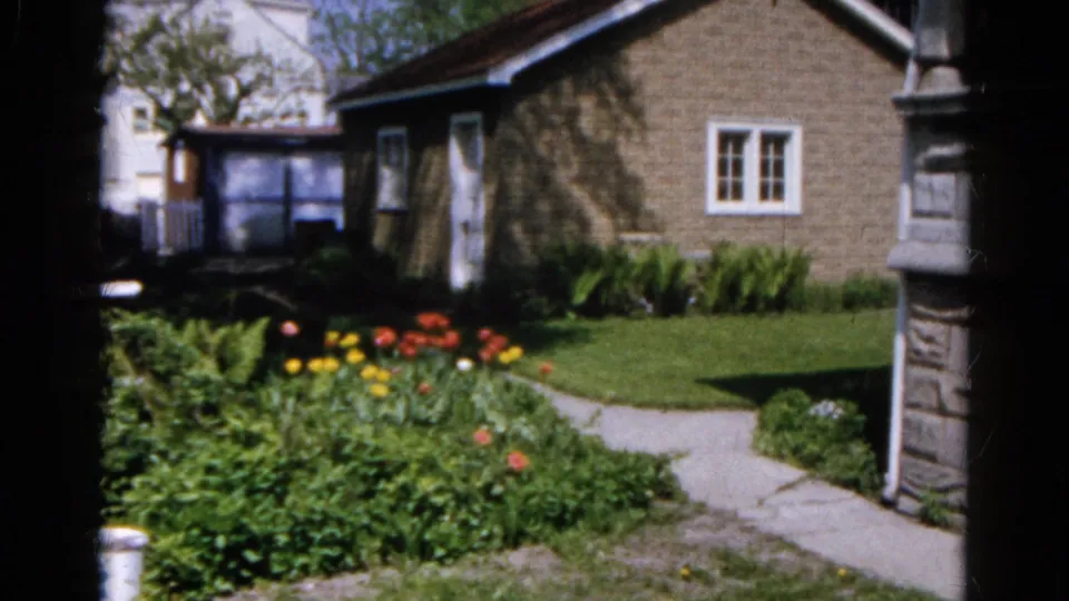 Brick house and garden in Wauconda, Illinois, 1961, with white-trimmed windows, lawn, flowers, and a walkway in 8mm color footage.