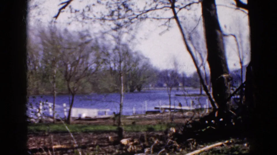 Wauconda lakeside scene from 1961, with dark foreground trees, a blue lake, docks, and a wooded opposite bank.