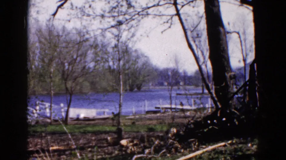 Soft-focus 1961 8mm lakeshore view in Wauconda, Illinois, with bare trees, blue water, docks, and shoreline brush.