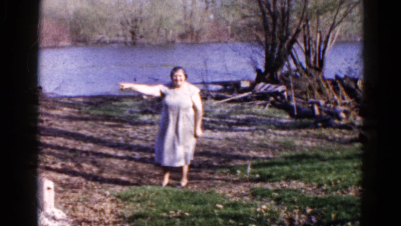 Woman in a light dress standing near a lake and pointing to the side.