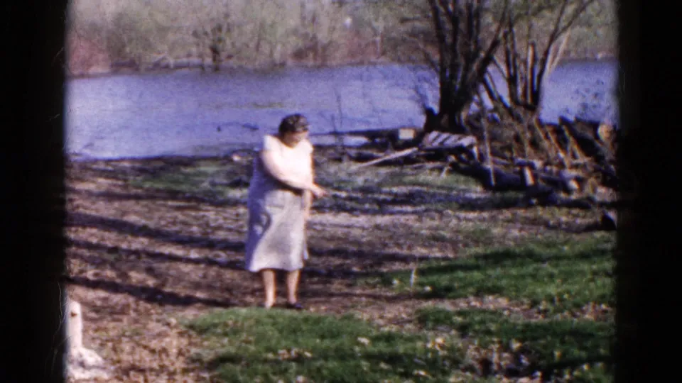 The woman turns partly away on the Wauconda lakeshore, with leafless trees, logs, and blue water in the background.