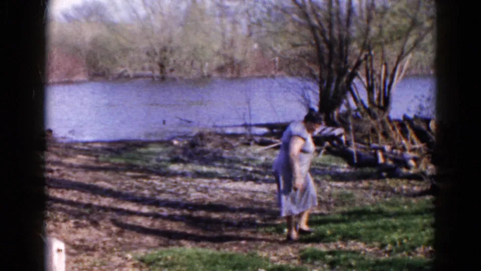 Adult woman bends slightly as she walks along the grassy riverbank in Wauconda, Illinois, 1961.