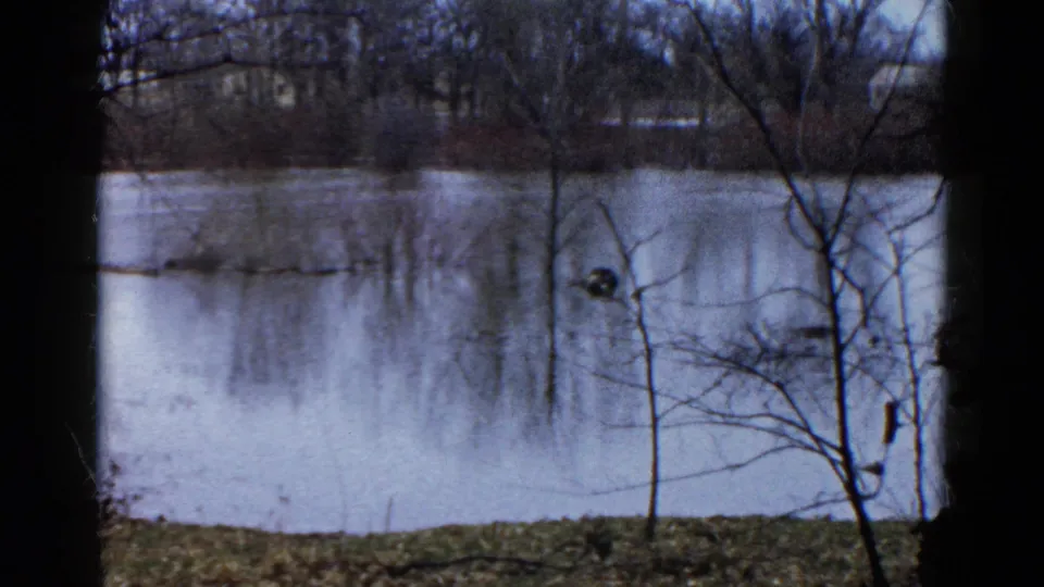 1961 Wauconda, Illinois 8mm view of a calm lake bordered by bare trees, with the seated person no longer clearly visible in this frame.