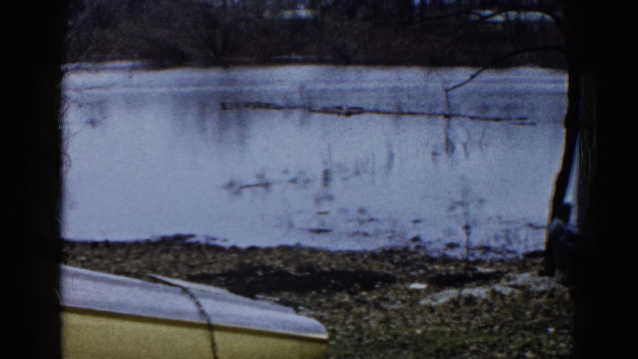 1961 Wauconda 8mm frame showing a frozen lakeshore, bare trees, and the edge of a yellow boat in the foreground.