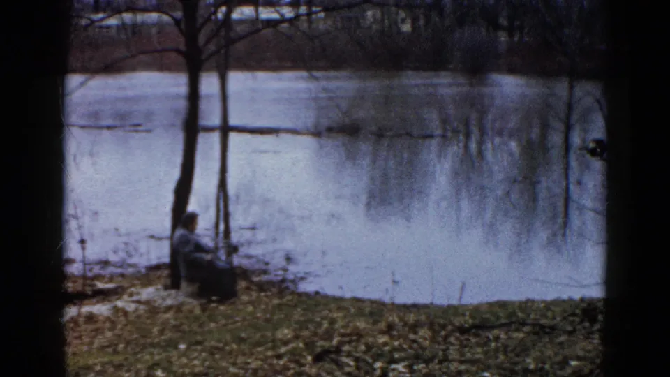 A seated person rests near two bare shoreline trees, with the partially frozen Wauconda lake behind them.