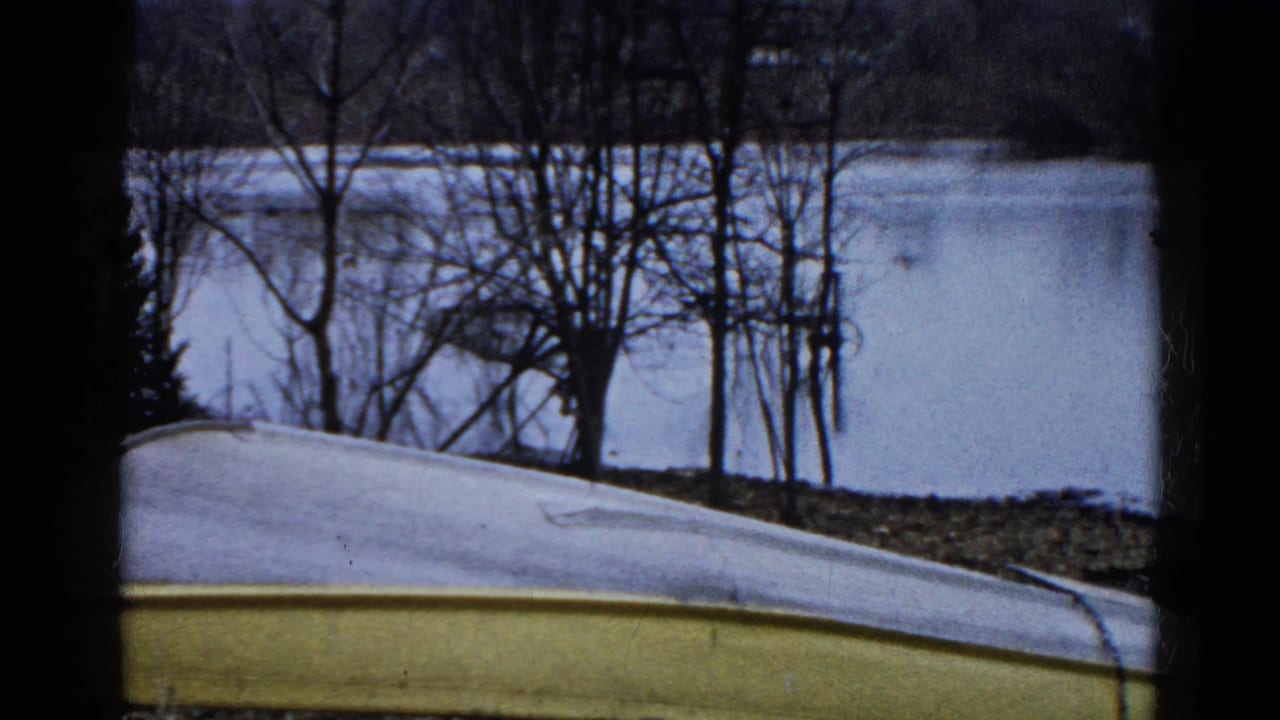 1961 Wauconda, Illinois 8mm frame showing an overturned yellow and white boat on a winter lakeshore with bare trees and still icy water.
