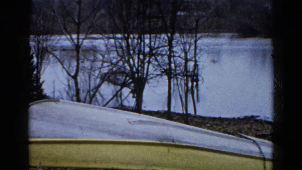 1961 Wauconda, Illinois 8mm frame showing an overturned yellow and white boat on a winter lakeshore with bare trees and still icy water.
