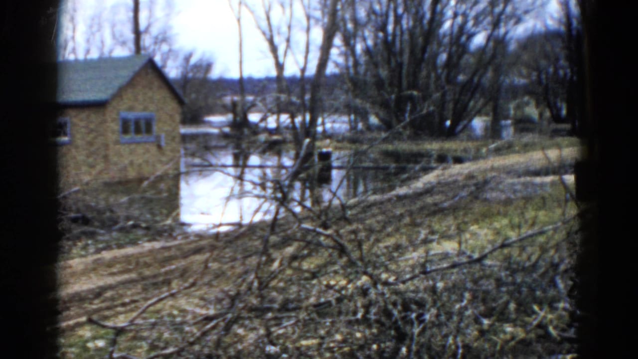 Brown lakeside building and calm water seen through bare trees and dark frame edges.