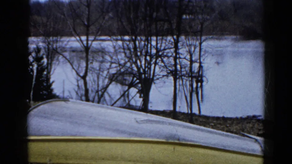 1961 Wauconda, Illinois 8mm frame showing still lake water, leafless trees, brush, and a pale curved foreground surface.