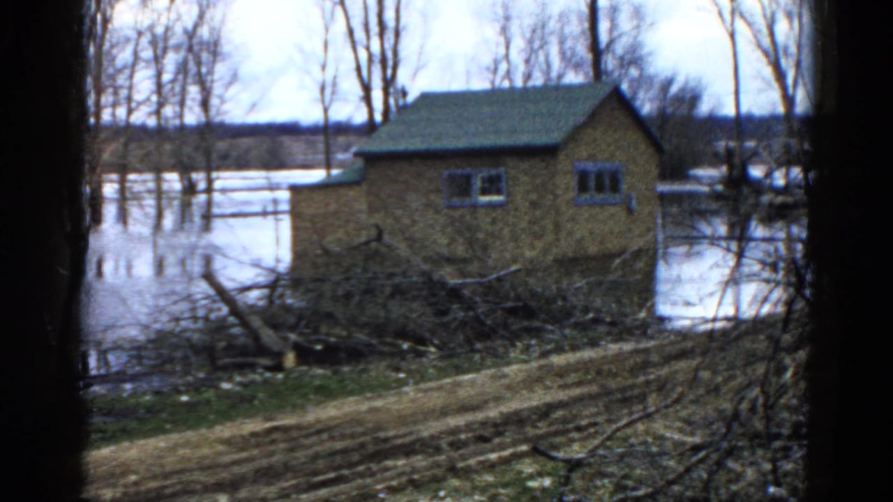 1961 Wauconda home-movie frame showing a small brick house partly surrounded by floodwater after a storm.
