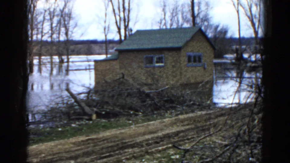 1961 Wauconda home-movie frame showing a small brick house partly surrounded by floodwater after a storm.