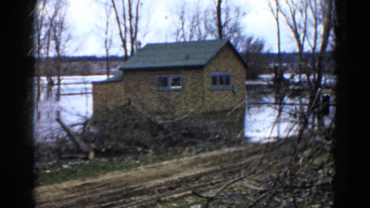 1961 Wauconda frame with a brick house, high water, muddy foreground, and storm debris in a rural setting.