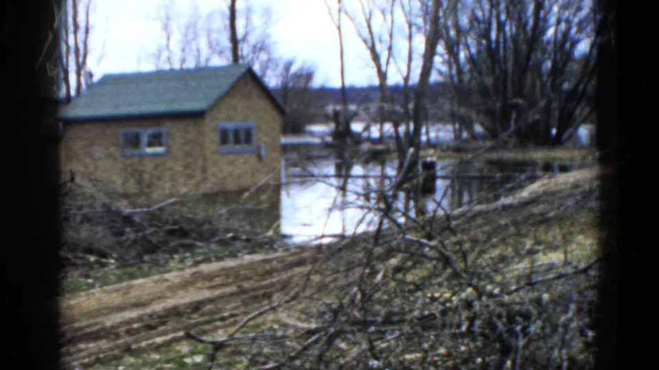 1961 Wauconda flood aftermath frame showing a small brick house, standing water, bare trees, and muddy ground.