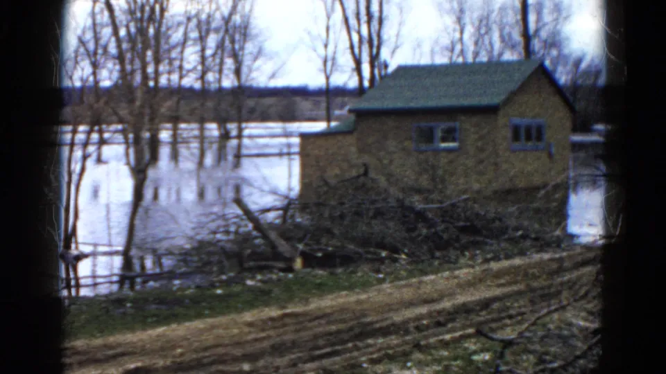 1961 Wauconda, Illinois 8mm still showing a small house-like structure, high water, leafless trees, brush, and a muddy bank.