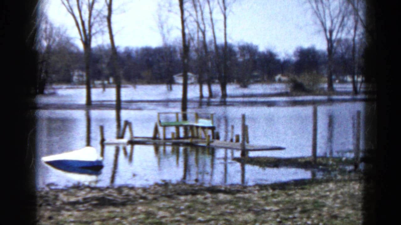 1961 Wauconda, Illinois home-movie frame showing a blue-and-white boat near a partly submerged dock on a flooded lakeshore.