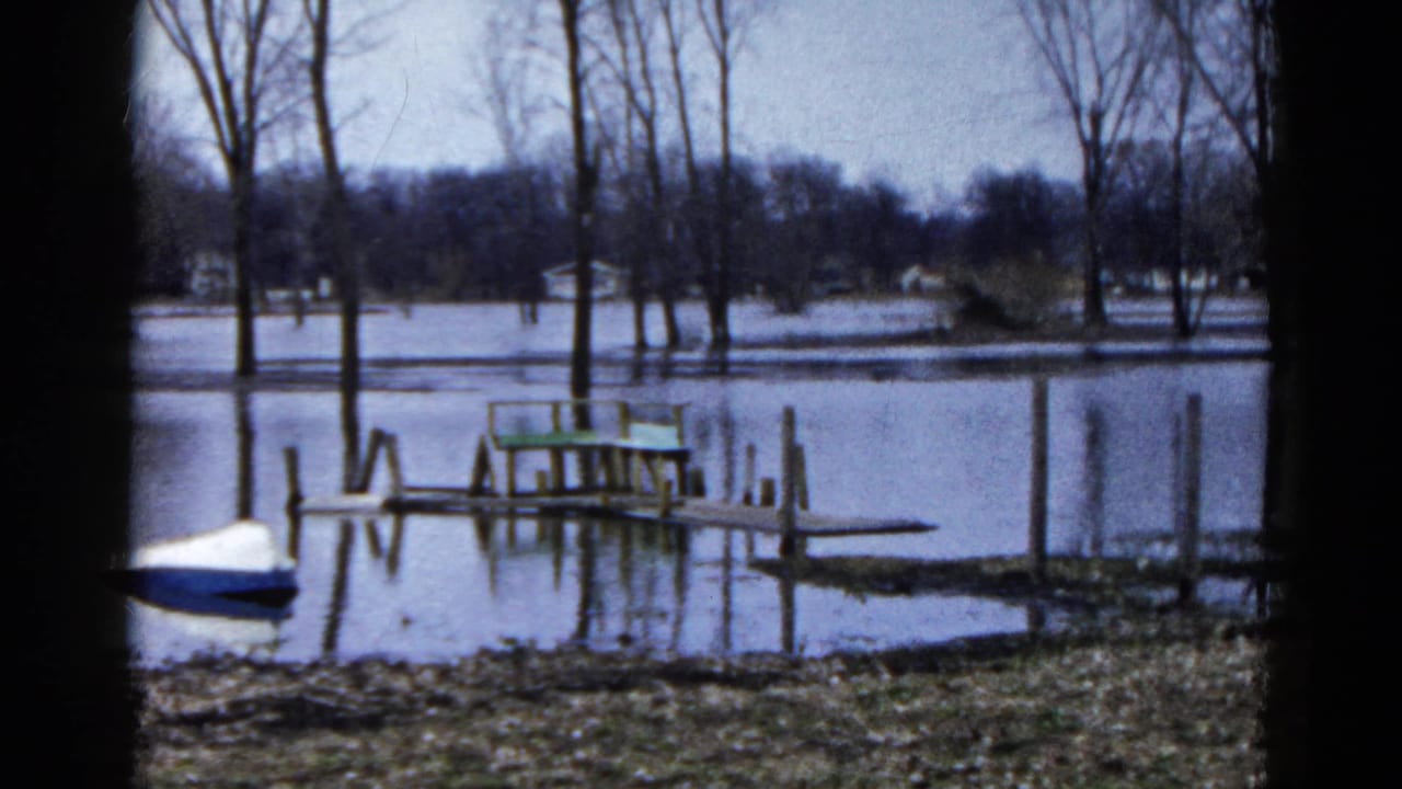 Flooded lakeside dock with a small blue-and-white boat at the left edge and trees beyond.