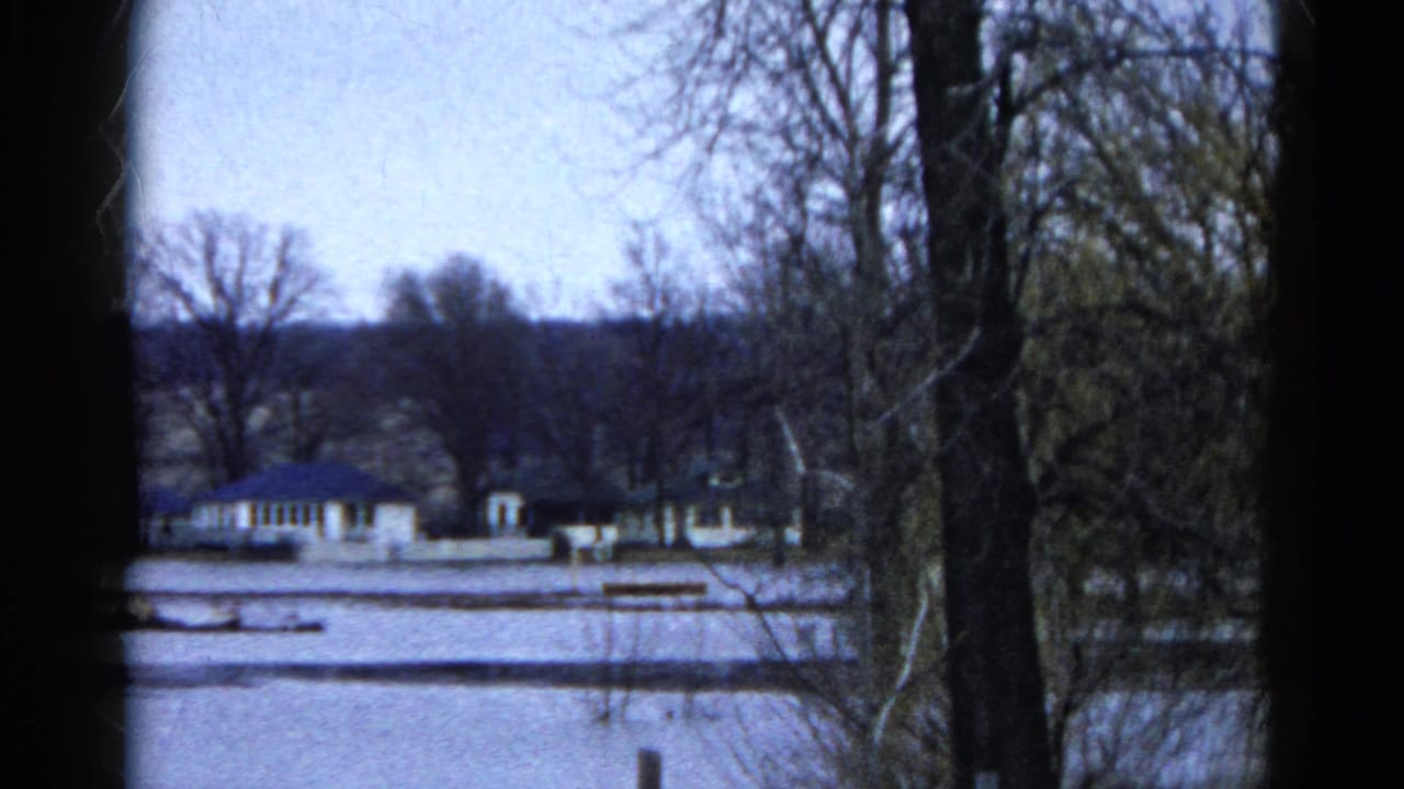 Bare trees frame distant buildings across a snow-covered open area.