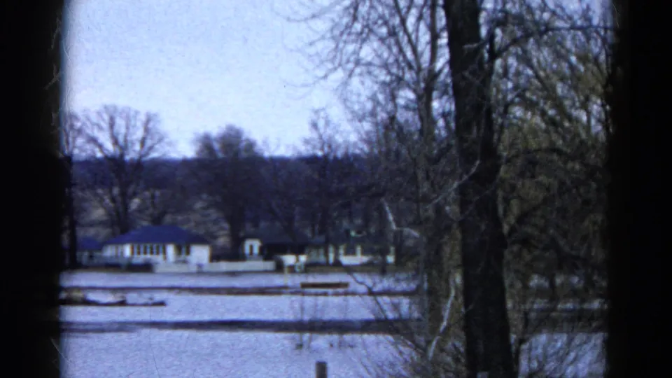 1961 Wauconda, Illinois 8mm frame showing floodwater, distant buildings, bare trees, and floating logs or debris.