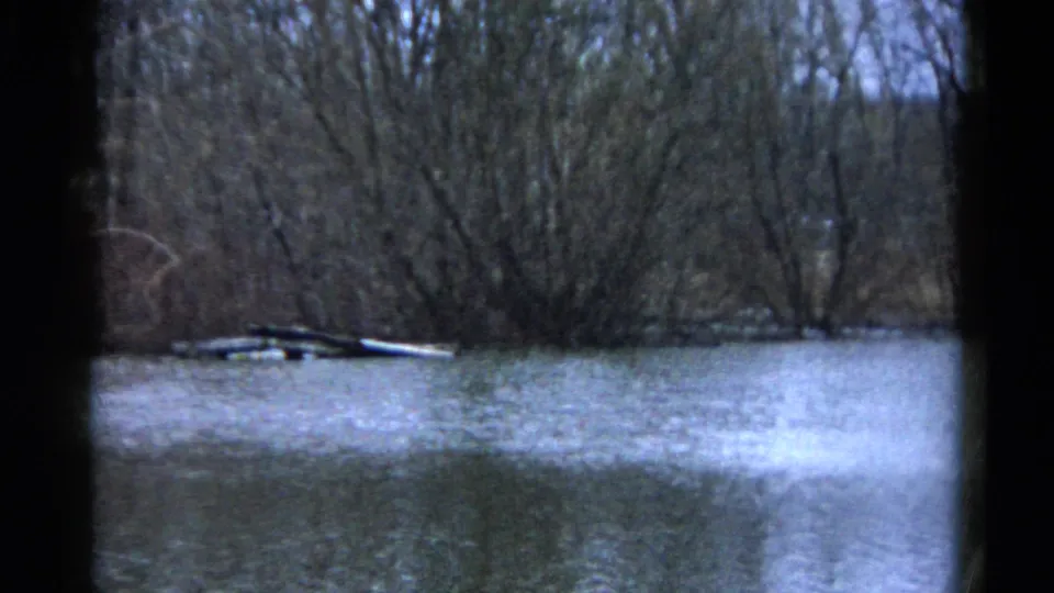 1961 Wauconda, Illinois frame showing still floodwater under bare trees, with debris along the bank and visible 8mm gate borders.