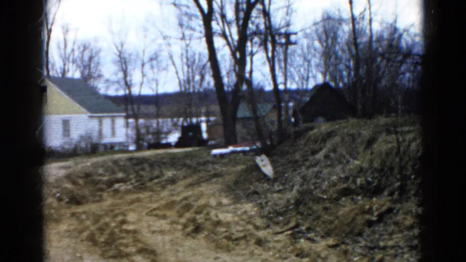 A closer home-movie view of the dirt path and bank, with the Wauconda lakeside house partly visible behind bare trees.