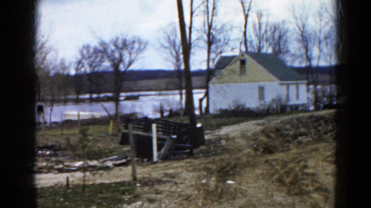 1961 Wauconda, Illinois 8mm frame showing a white house with yellow gable near flooded lake water and leafless trees.