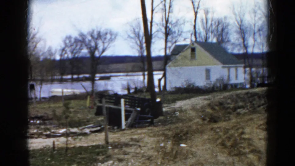 1961 Wauconda, Illinois 8mm frame showing a white house with yellow gable near flooded lake water and leafless trees.