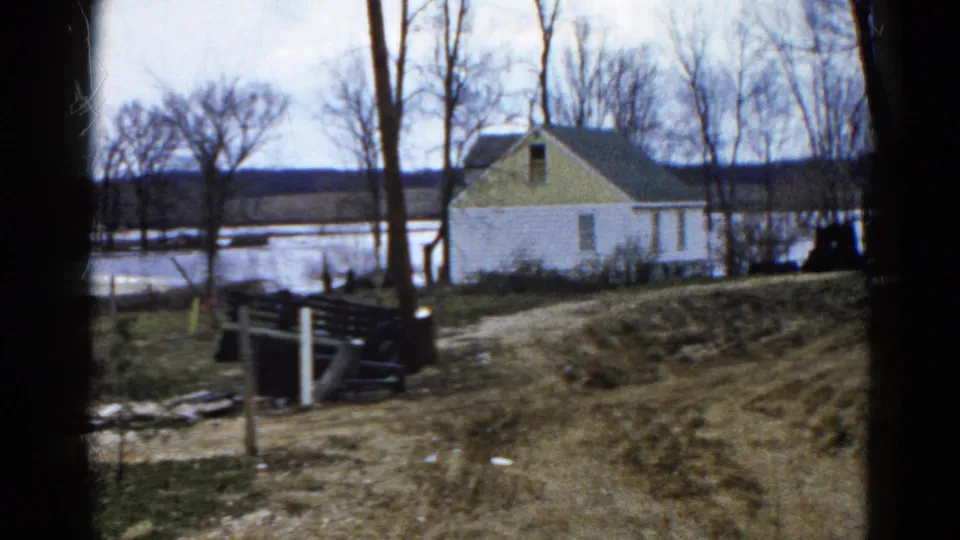 The pan continues across the Wauconda lakeside house, with leafless trees, wet ground, and distant shoreline visible.