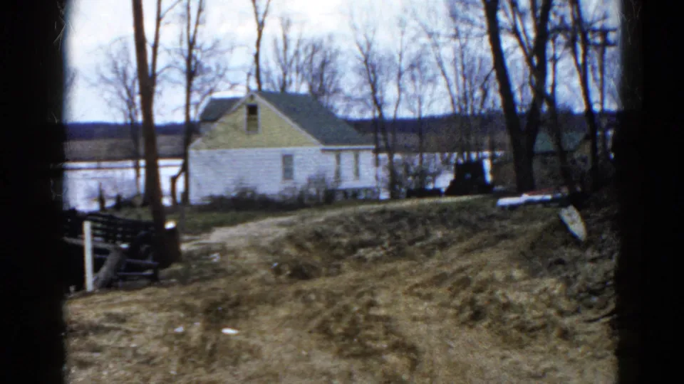 Final frame of the 1961 Wauconda pan holds on the lakeside house, leafless trees, muddy ground, and pale overcast sky.