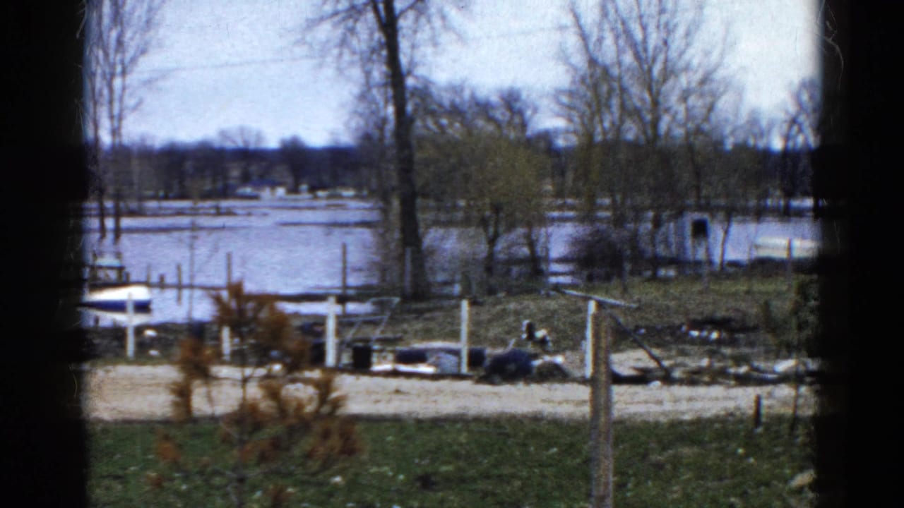 1961 Wauconda, Illinois 8mm frame showing a flooded shoreline with submerged dock sections, boats, and bare trees.