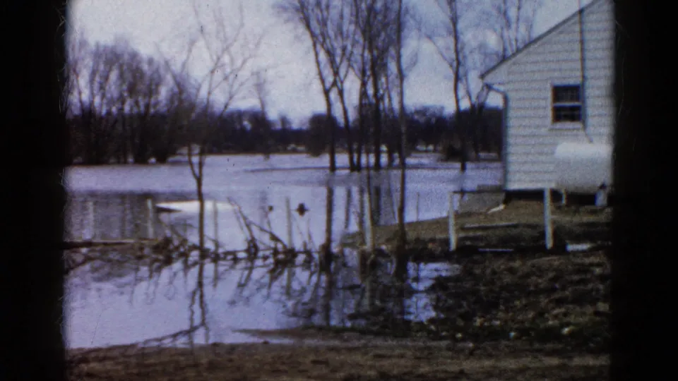 A white house stands beside high floodwater and leafless trees in this 1961 Wauconda, Illinois home-movie frame.