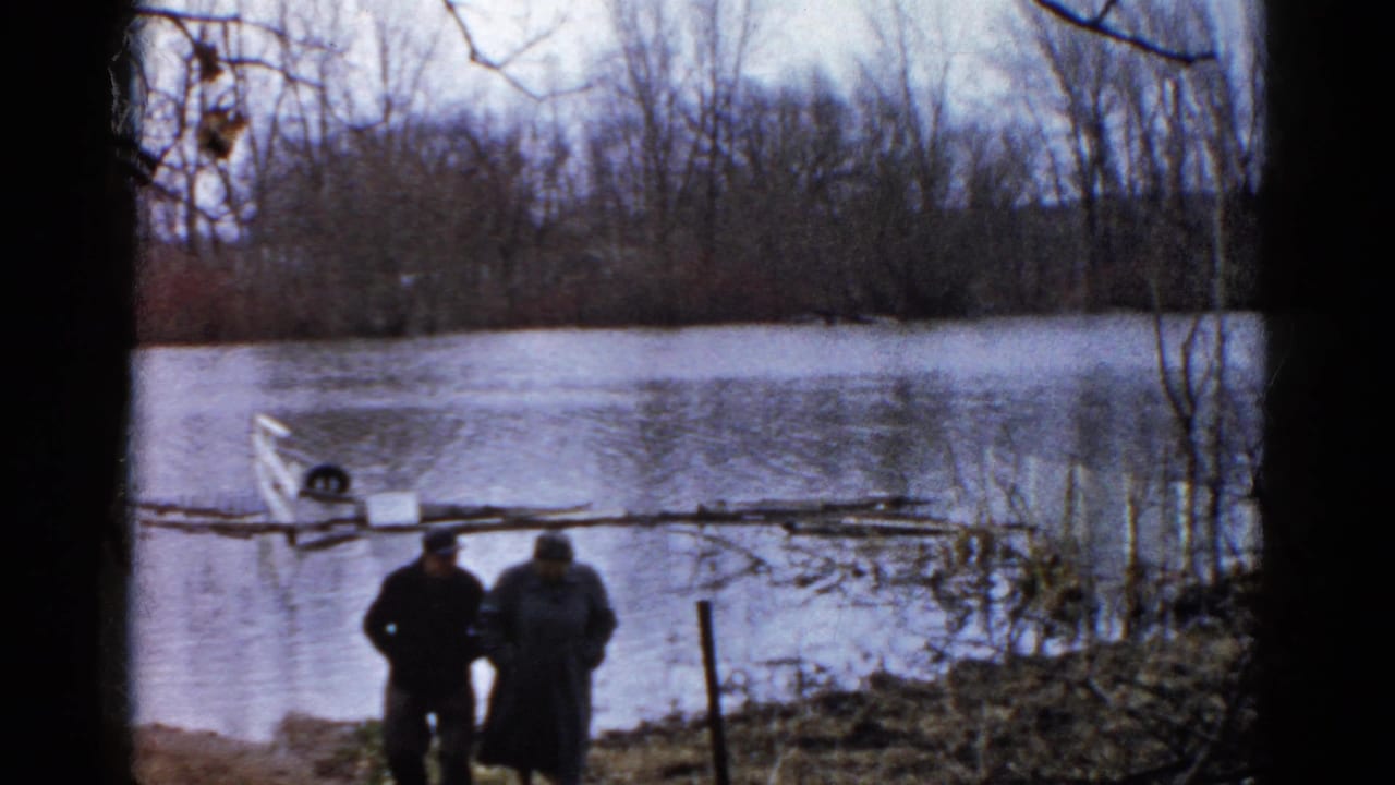 Two men stand near a flooded shoreline with a small partly submerged boat behind them.