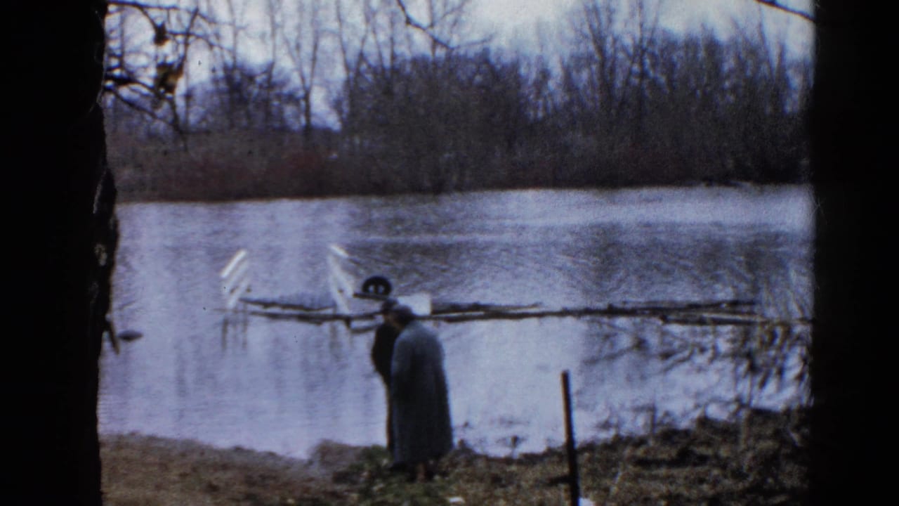 In supplied 1961 Wauconda, Illinois context, two bundled adults stand by a flooded pond with bare trees and a partly submerged object nearby.