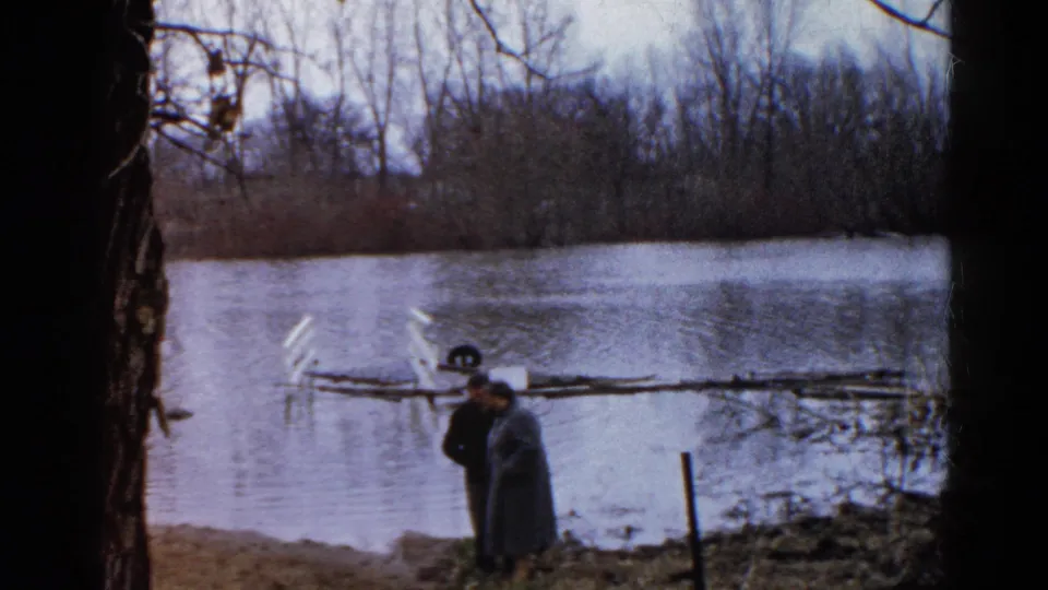 Two adults appear to converse near the flooded pond in Wauconda, Illinois, with bare trees and debris or a small structure in the water.