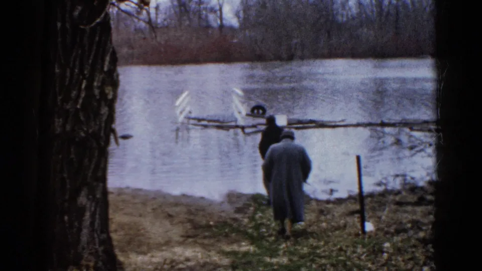 1961 Wauconda lakeside view with two adult men near the shore and a dark foreground tree trunk.