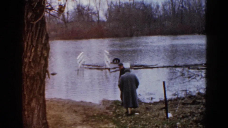 Two adult men at a cloudy Wauconda lakeshore in 1961, with bare trees and water behind them.
