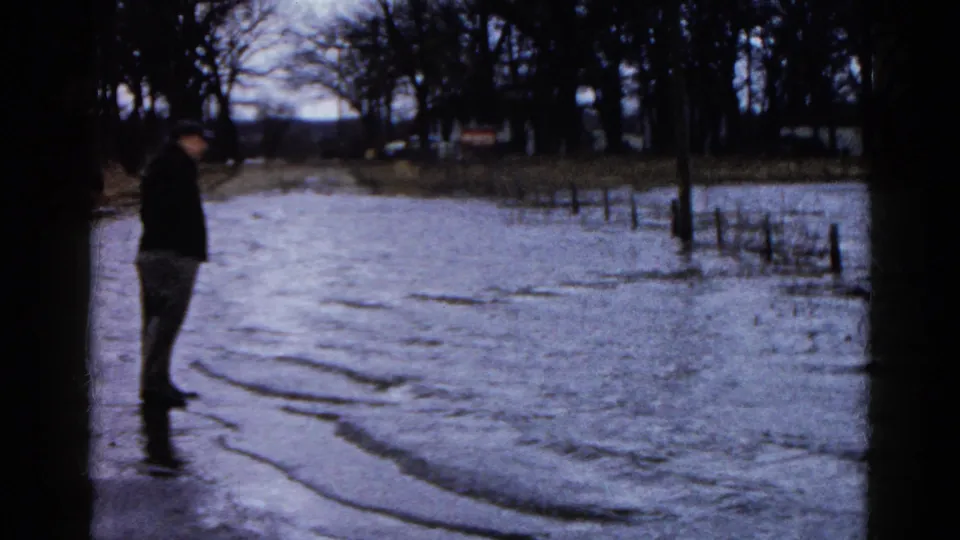A man in profile surveys floodwater over rural ground in Wauconda, Illinois, in a 1961 8mm home-movie frame.