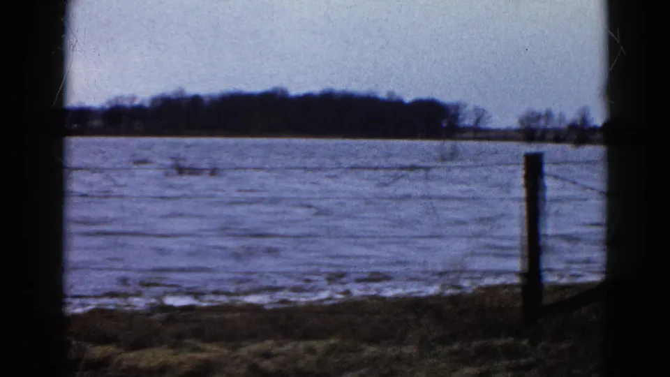 A wider 1961 rural Wauconda view shows water spread across the field, with a fence post near the edge and bare trees along the horizon.