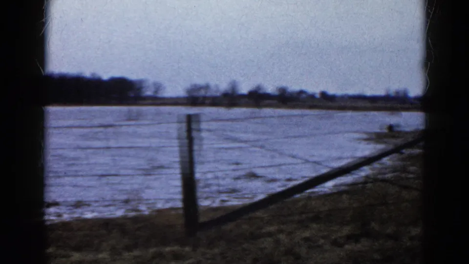 At the end of the pan, floodwater fills the rural Wauconda field while a fence post and diagonal rail or wire cross the foreground.