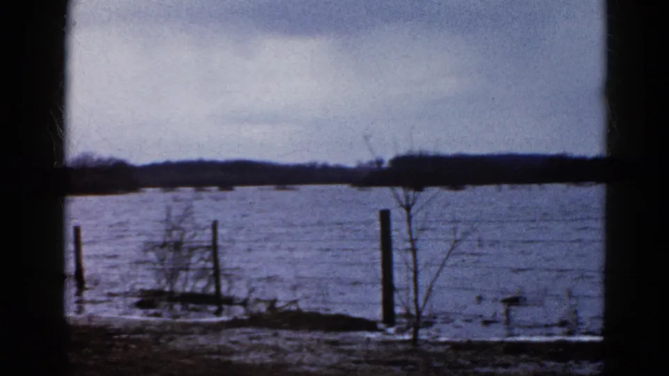 8mm home-movie view of Wauconda floodwater covering low ground beside a road and fence line in 1961.