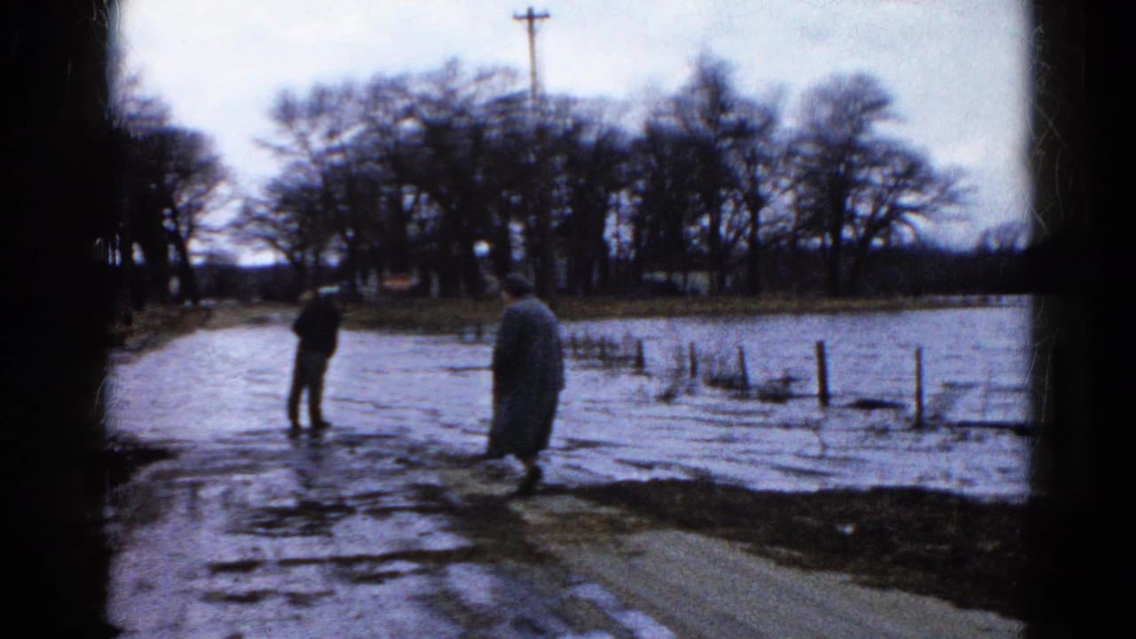 Two adults in coats observe floodwater along a rural road in Wauconda, Illinois, based on supplied 1961 metadata.