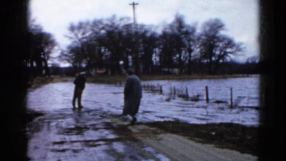 Two adults in coats observe floodwater along a rural road in Wauconda, Illinois, based on supplied 1961 metadata.