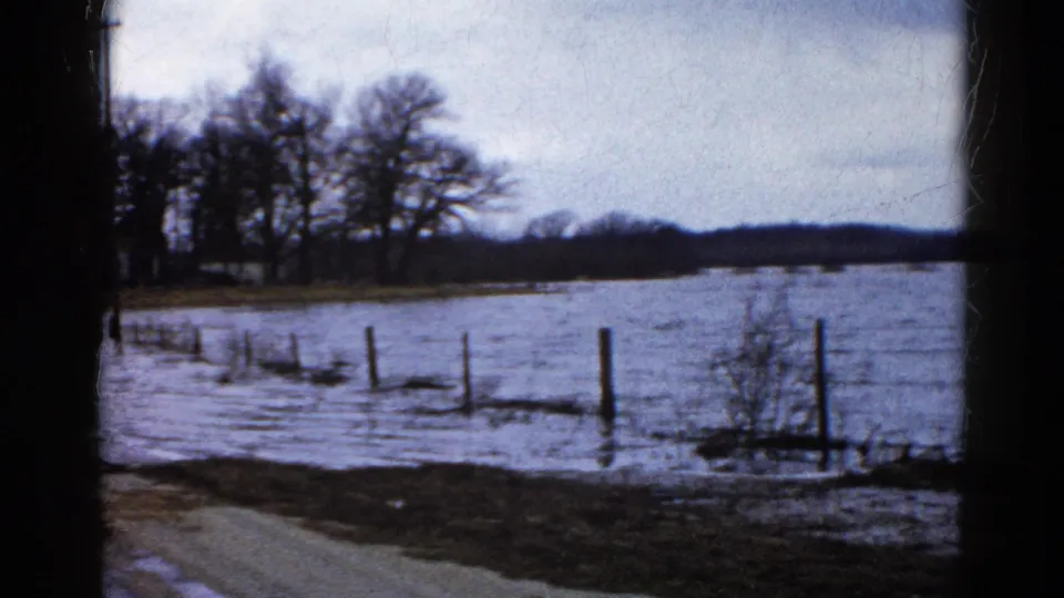 Floodwater spreads across a rural field and fence line in Wauconda, Illinois, with the people now mostly out of view.