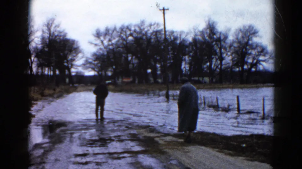 In the Wauconda, Illinois footage, the man looks toward water across the pavement as the woman waits near the edge of the flooded road.