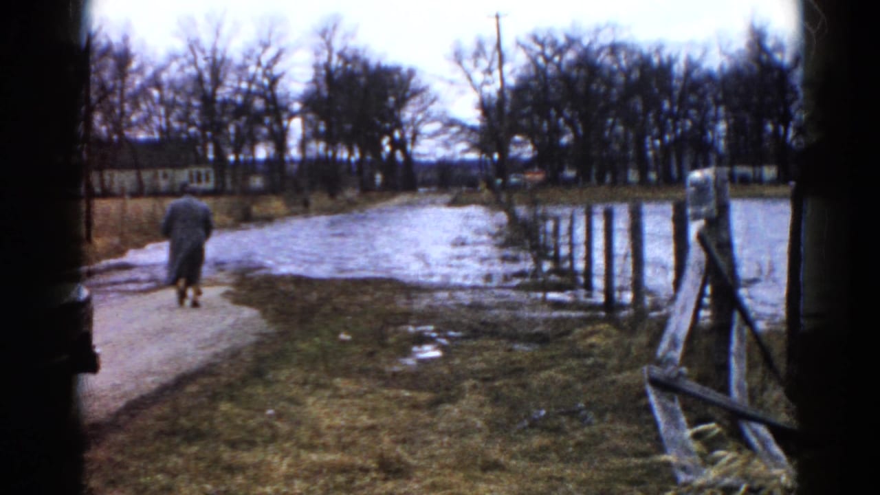 Two coat-wearing adults continue away from the camera on a path beside water.