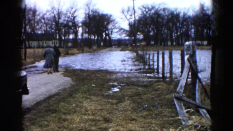 At the end of the clip, the adults continue down the wet Wauconda walkway, with high water, bare trees, and a wooden fence visible.