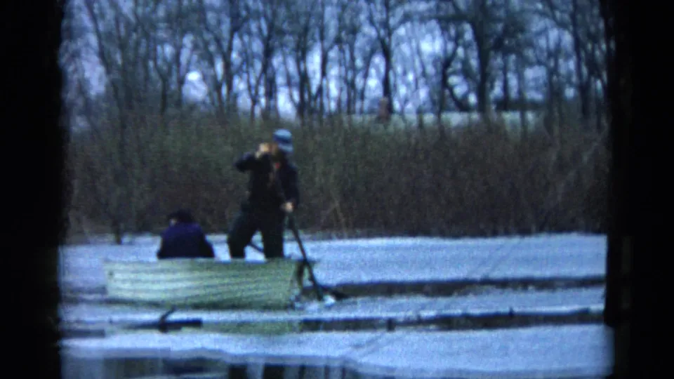 A standing person rows a pale boat while another sits forward on a calm Wauconda lake in 1961 home-movie footage.