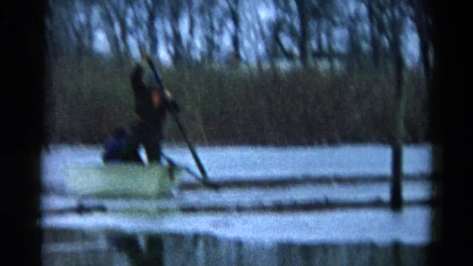 Soft, motion-blurred 1961 Wauconda frame showing the small boat and rower on still lake water near a dark shoreline post.