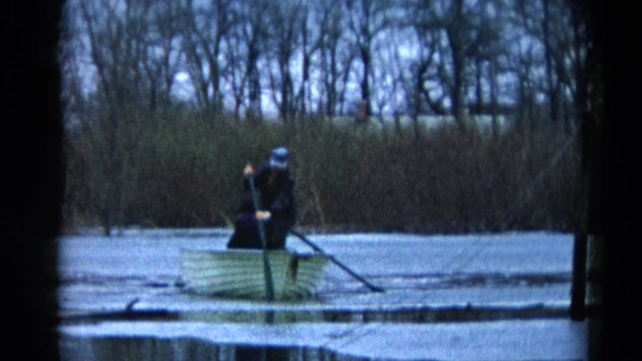 In Wauconda, Illinois, 1961, a man in dark clothing stands in a rowboat on a frozen pond and works an oar through thin ice.